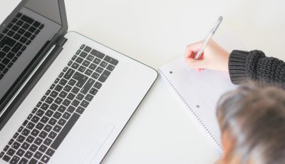 Kuvituskuva henkilöstä, joka katsoo kannettavan tietokoneen näyttöä ja tekee kynällä muistiinpanoja paperille.