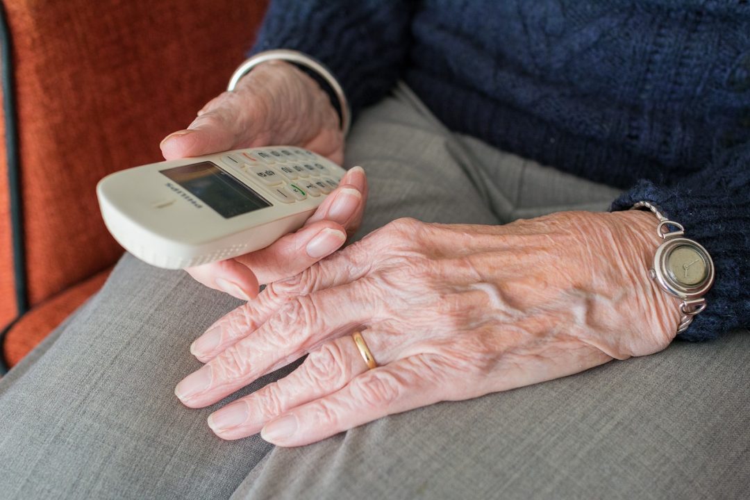 Kuvituskuva vanhan ihmisen käsistä, jotka pitelevät yksinkertaista matkapuhelinta.